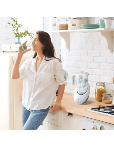 Mujer bebiendo agua junto a una jarra hidrogenadora en la cocina