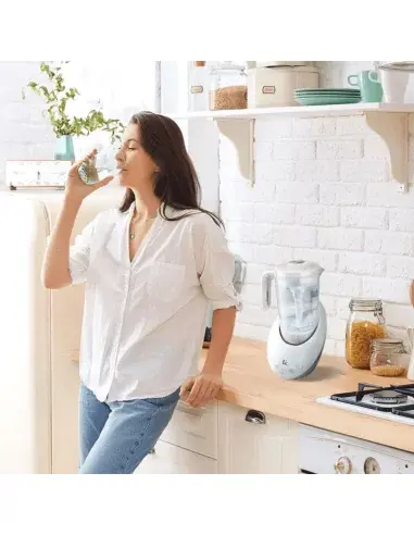 Mujer bebiendo agua junto a una jarra hidrogenadora en la cocina